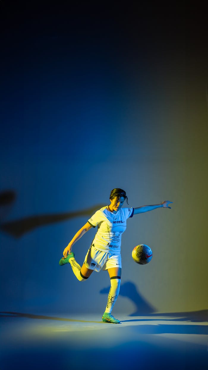 Woman soccer player kicks ball in a vibrant studio setting.